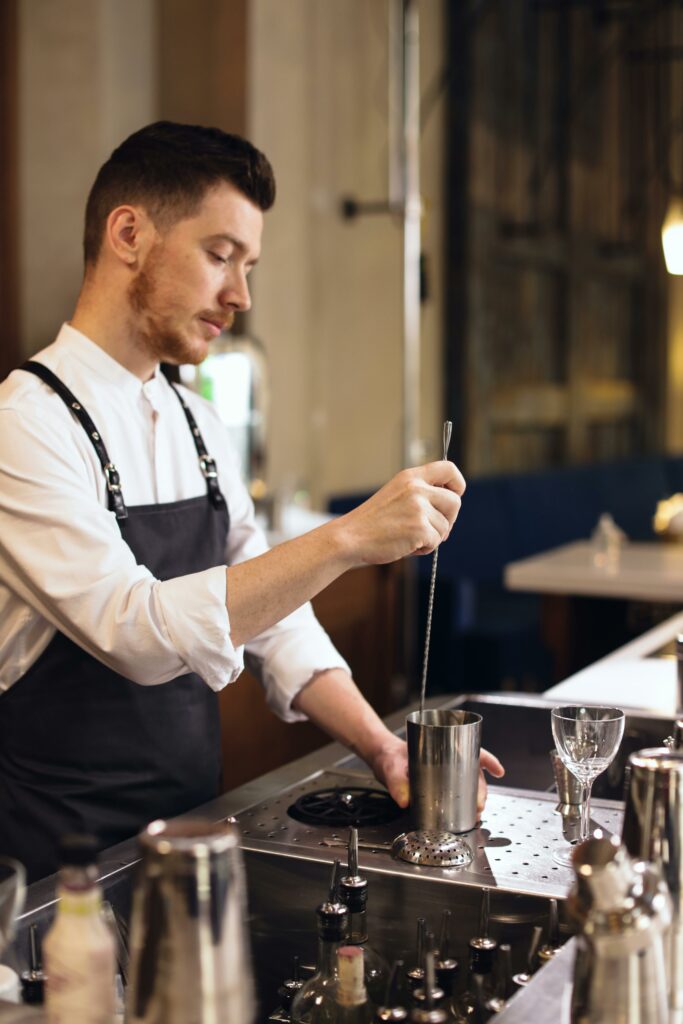 A focused bartender mixes a cocktail at an upscale bar, demonstrating skilled bartending techniques.