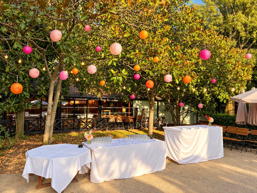 Lampions roses et oranges suspendus dans les magnolias, tables de cocktail dressees